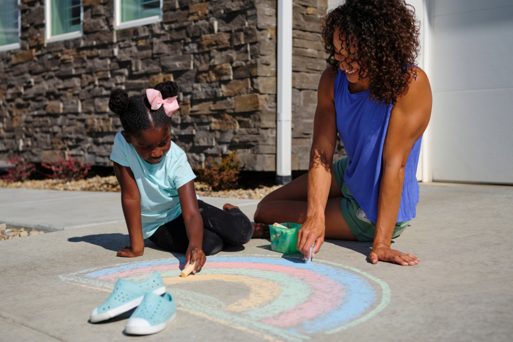 Mom girl drawing rainbow with sidewalk chalk